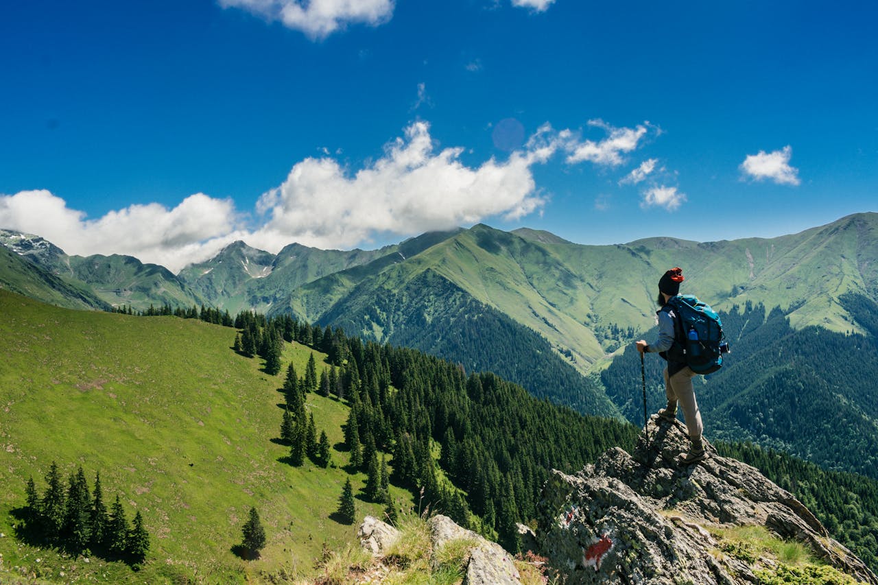 about-01 Adventurous hiker enjoying breathtaking views of lush green mountains in Romania under a clear blue sky.