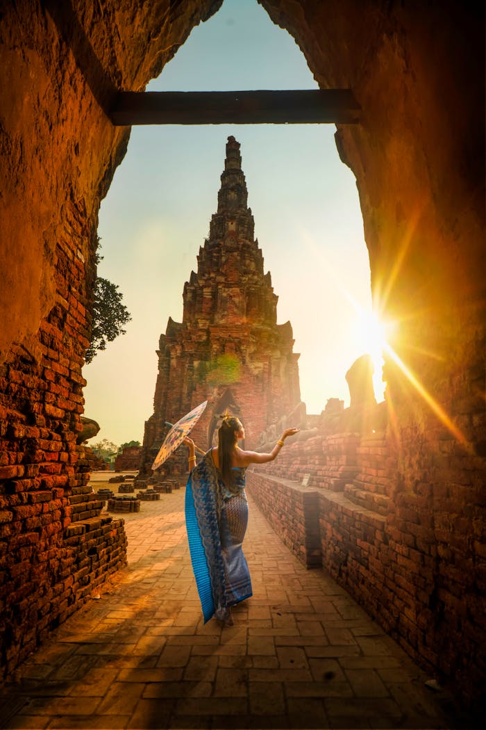 our-services-3 A woman in traditional wear stands with an umbrella at a historic Ayutthaya temple during sunset.