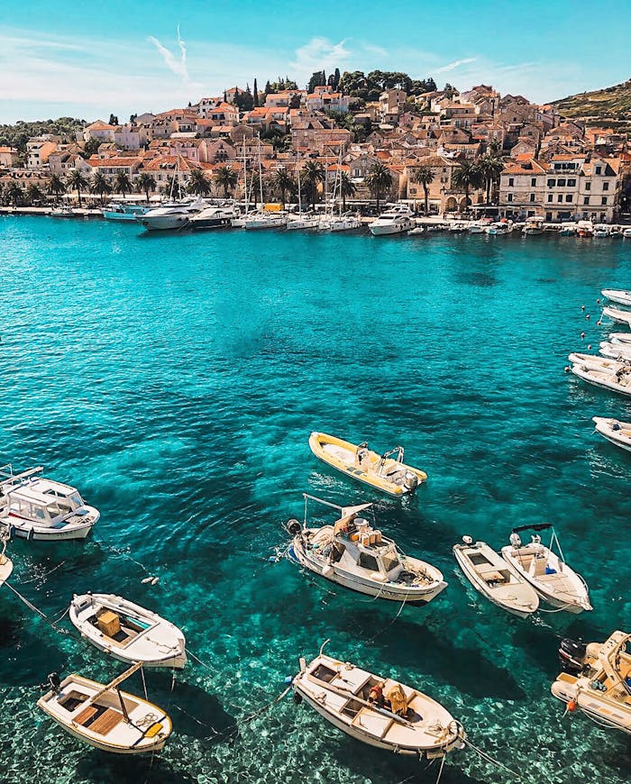 our-services-2 Boats in the vibrant blue waters of Hvar, Croatia, showcasing a charming coastal town under sunny skies.