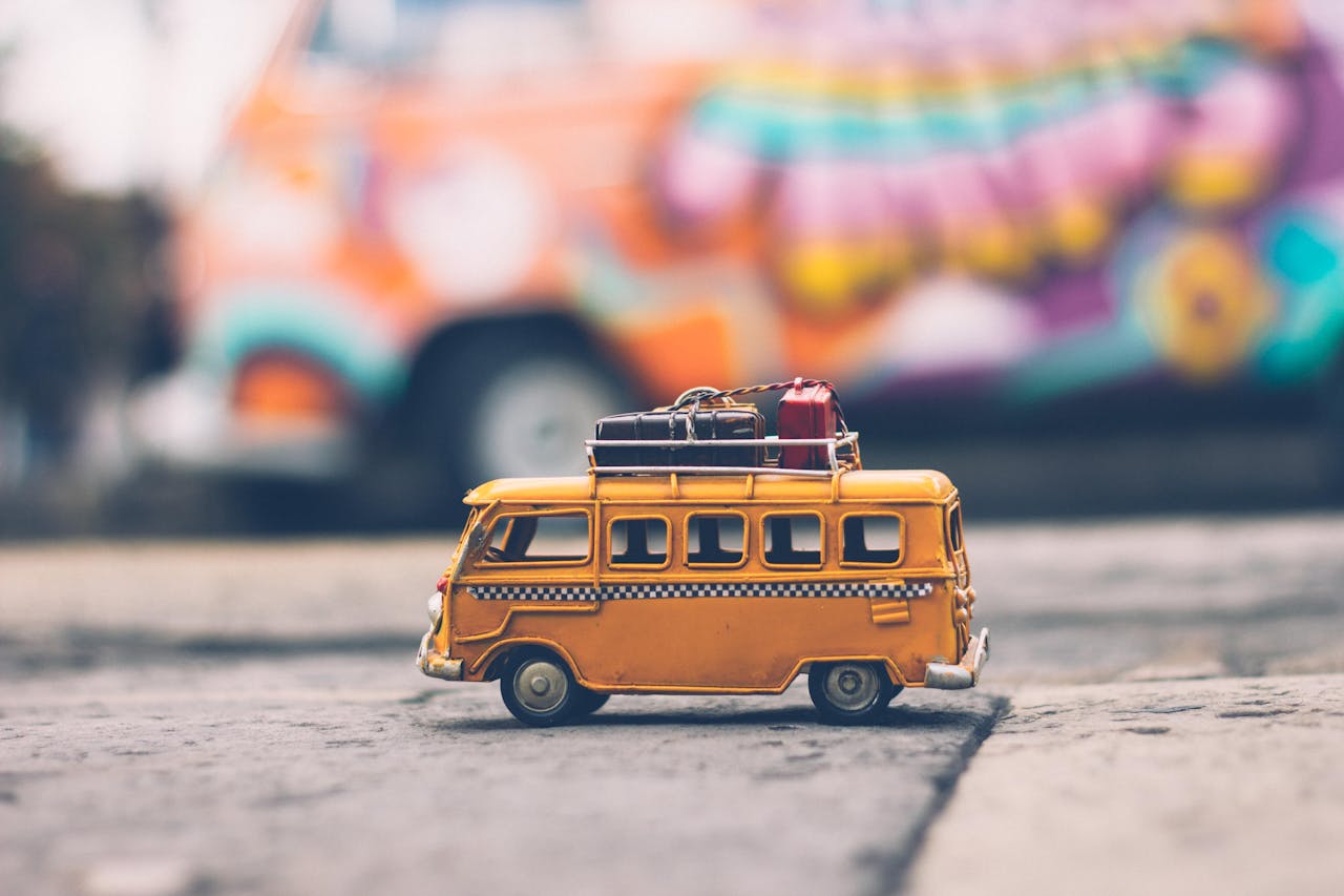 gallery-2 Close-up of a toy Volkswagen van with luggage, set against a colorful street backdrop, evoking summer travel vibes.